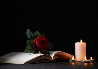 front view burning candles with open book red flower dark surface
